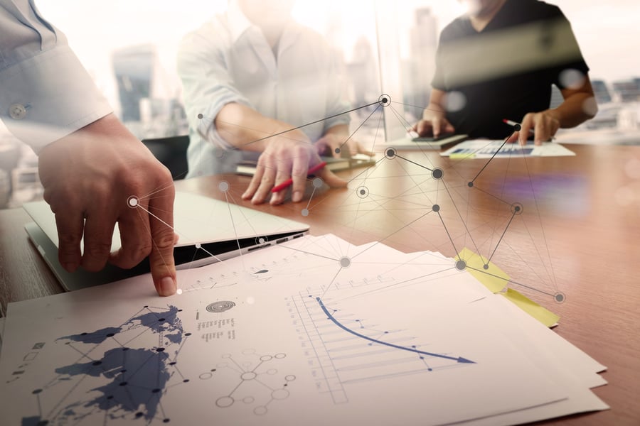 business documents on office table with smart phone and laptop computer and graph financial with social network diagram and two colleagues discussing data in the background